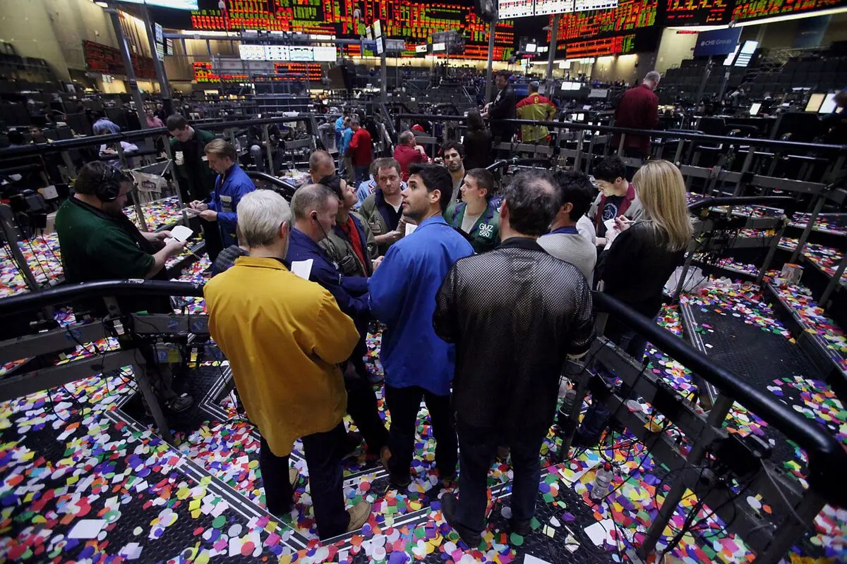 Traders standing on a confetti-covered trading floor with electronic ticker boards in the background.