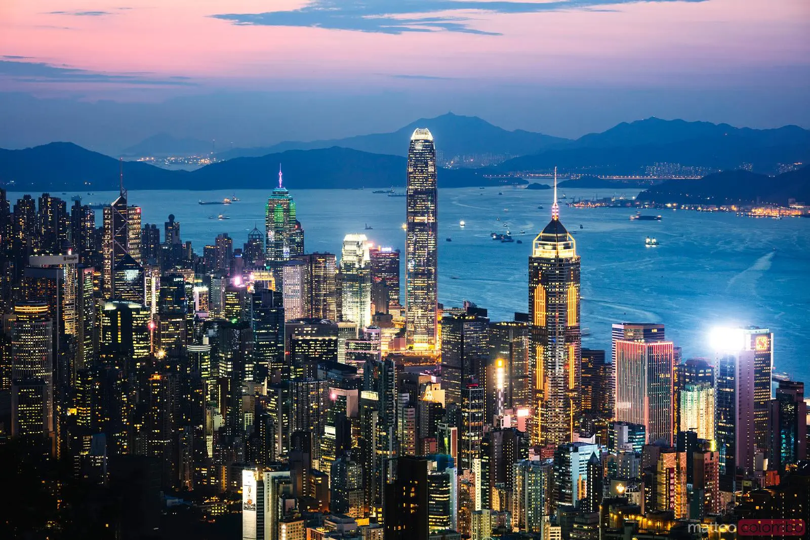 Aerial night view of the Hong Kong financial district skyline with illuminated skyscrapers and Victoria Harbour