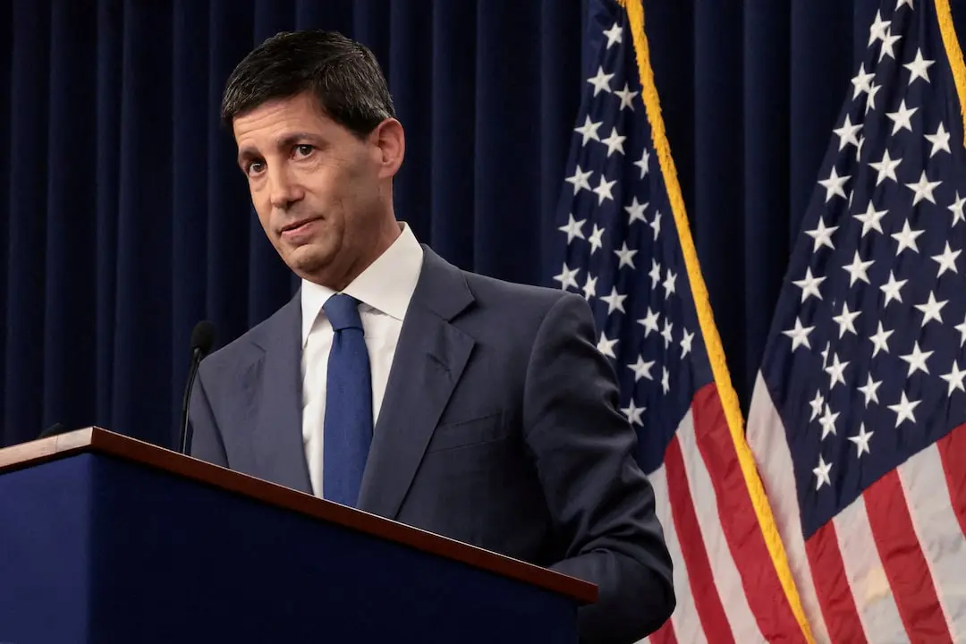 Kevin Warsh speaking at a podium in front of American flags