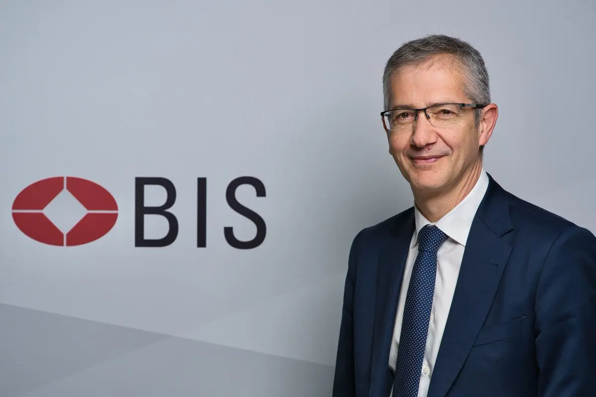 Portrait of Pablo Hernandez de Cos smiling in a navy suit and tie, standing next to the BIS logo