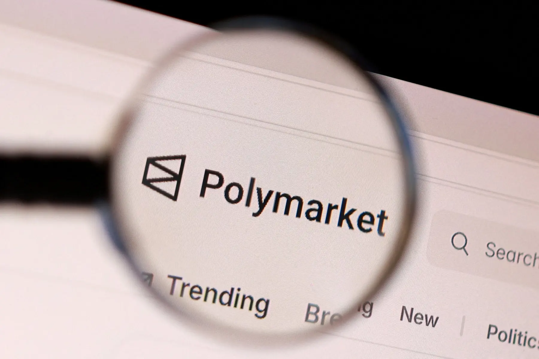 A magnifying glass focusing on the Polymarket logo and website header on a digital screen
