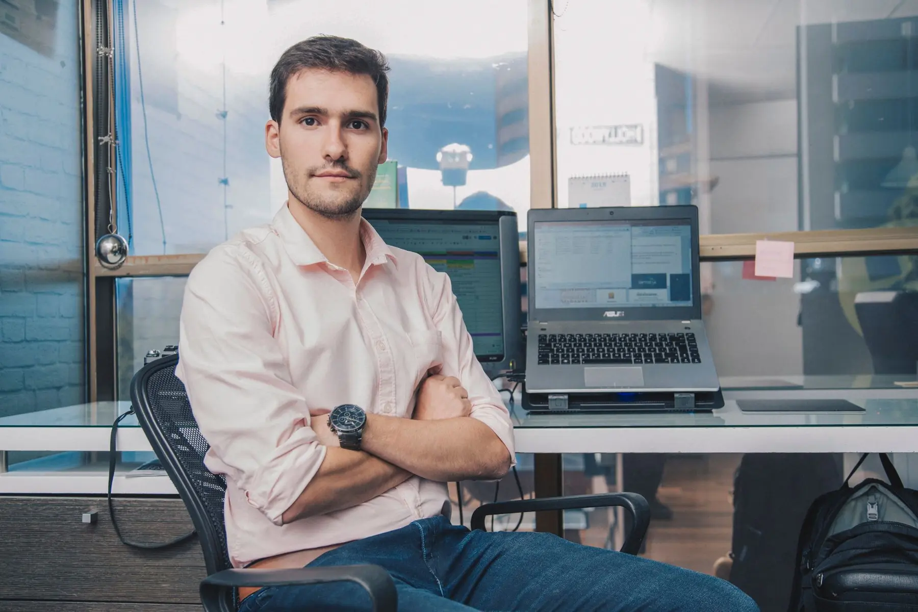 Andre Dragosch sitting in an office chair with arms crossed in front of a laptop and monitor.