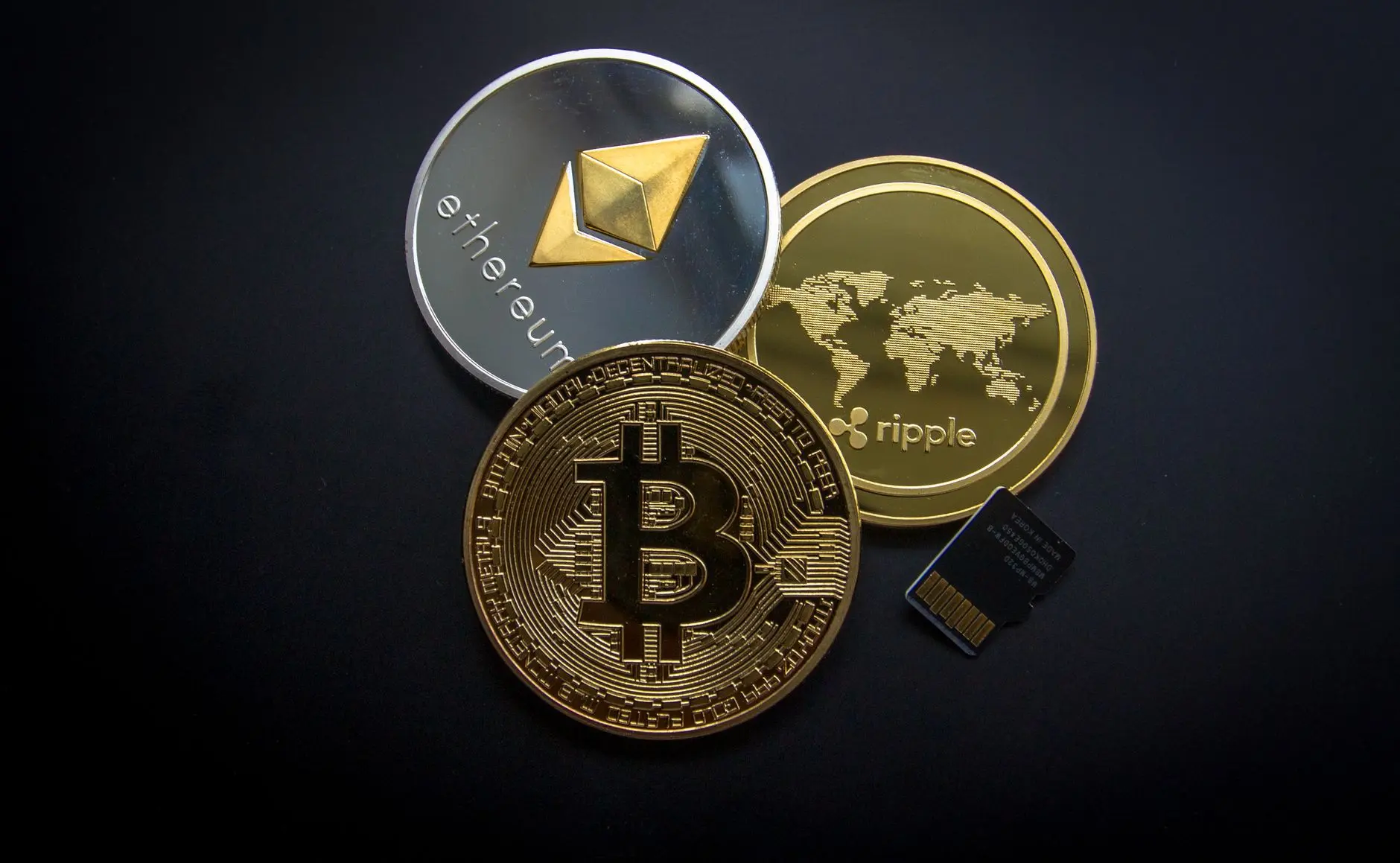 Physical Bitcoin, Ethereum, and Ripple cryptocurrency coins resting on a black surface