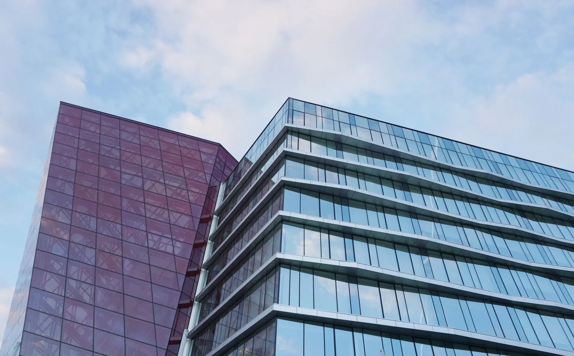 Modern office architecture featuring a glass facade building next to a red geometric structure under a blue sky