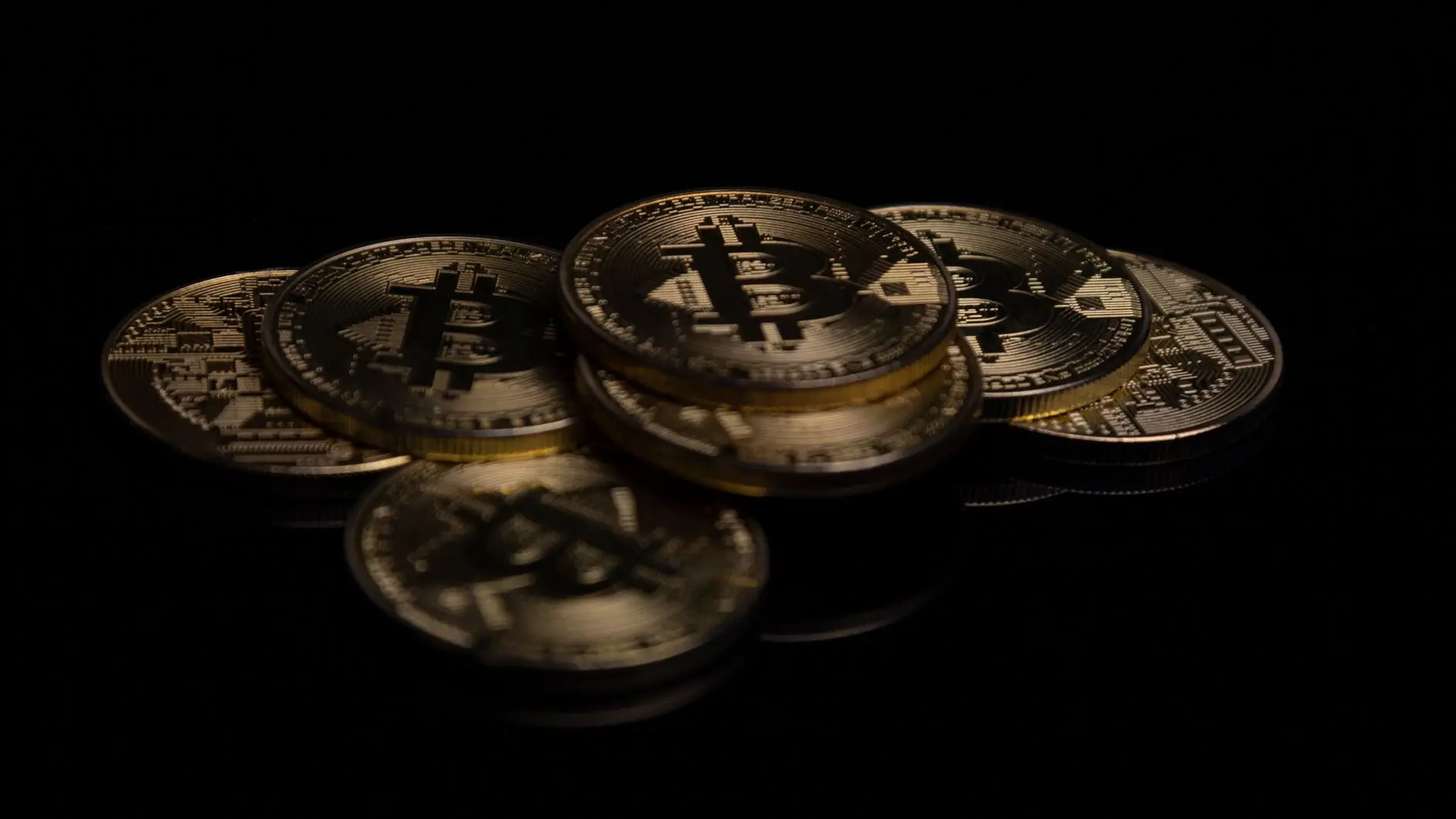 A stack of physical gold-colored Bitcoin coins on a reflective black surface