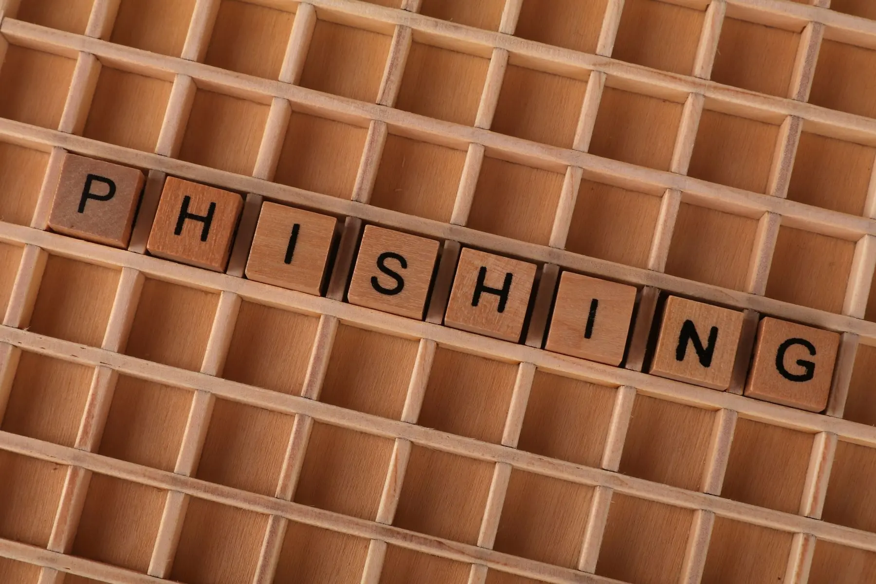 Wooden letter blocks spelling PHISHING arranged in a wooden grid tray