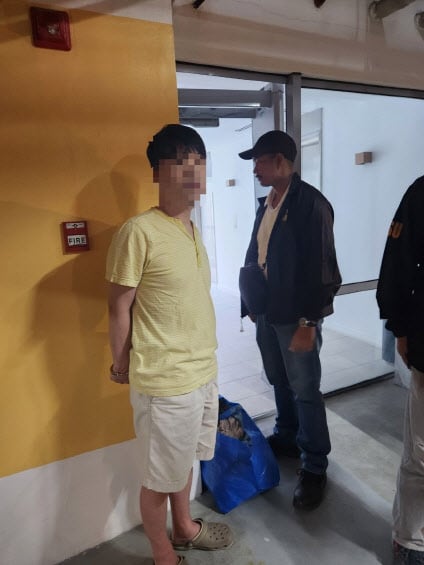 A man suspected of stealing money from South Korea in handcuffs, with a police officer in the background.