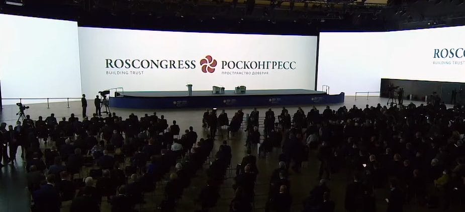 قاعة محاضرات كبيرة معتمة من جهة الحضور مع شاشة سوداء تعرض كلمات وشعار منظّمة