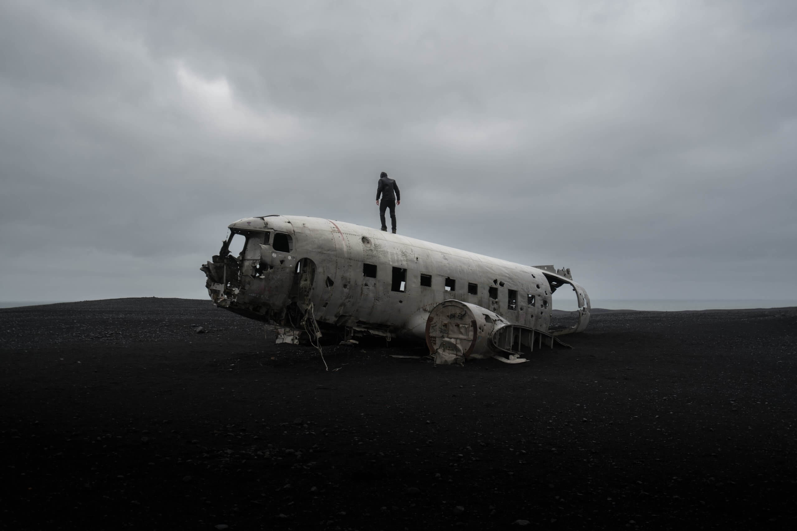 person standing on wrecked airplane under gloomy sky