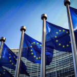 Rows of European Union flags are displayed outside the European Commission headquarters in Brussels, symbolizing the EU’s policymaking presence - Cover art/illustration via CryptoSlate.
