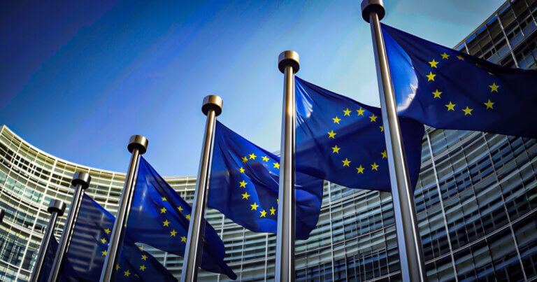 Rows of European Union flags are displayed outside the European Commission headquarters in Brussels, symbolizing the EU’s policymaking presence - Cover art/illustration via CryptoSlate.