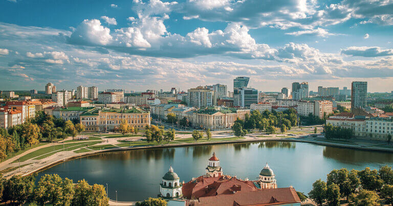 A cityscape view of Minsk, Belarus, shows historic architecture alongside modern buildings under a partly cloudy sky - Cover art/illustration via CryptoSlate.