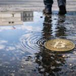 A Bitcoin coin ripples in a puddle reflecting a US government building as a passerby walks past, symbolizing how Trump and Powell political tensions could impact Bitcoin markets