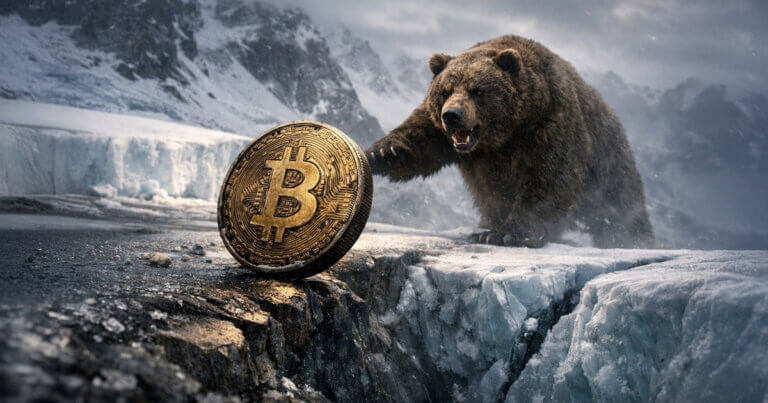 Bitcoin coin on an icy ledge as a bear prowls across a frozen crevasse, symbolizing a bear-market bottom nearing a buy zone with more downside risk ahead