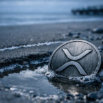 XRP coin partially submerged in a shallow tide pool on a dark beach, reflecting a sharp weekend price dip in the cryptocurrency market